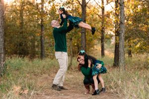 Playful family photoshoot in autumn forest with golden sunlight filtering through trees.