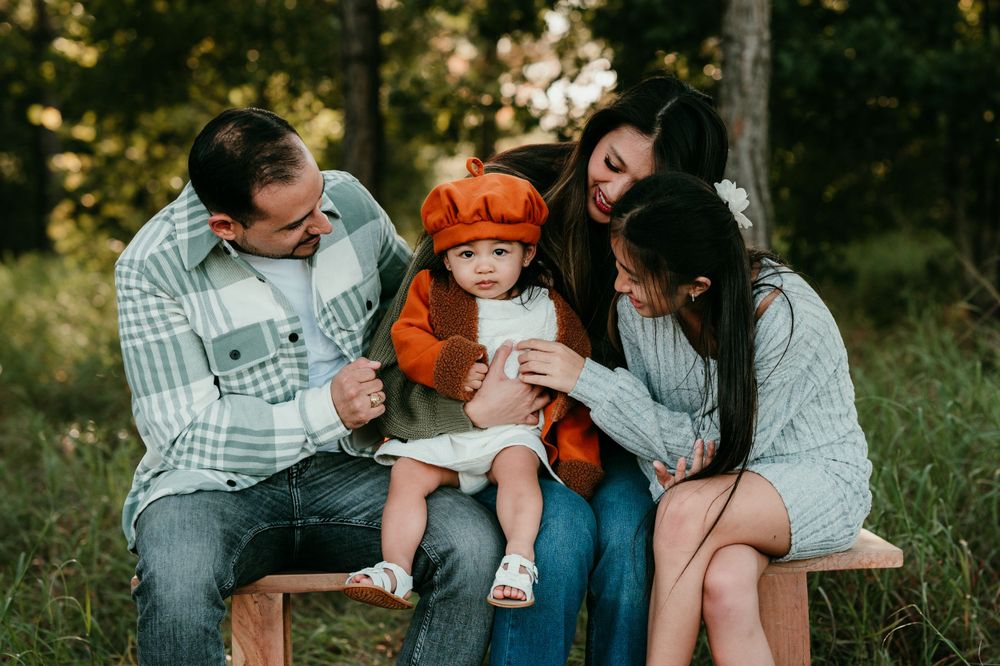 Family sitting together on a wooden bench during golden hour in a forest setting.