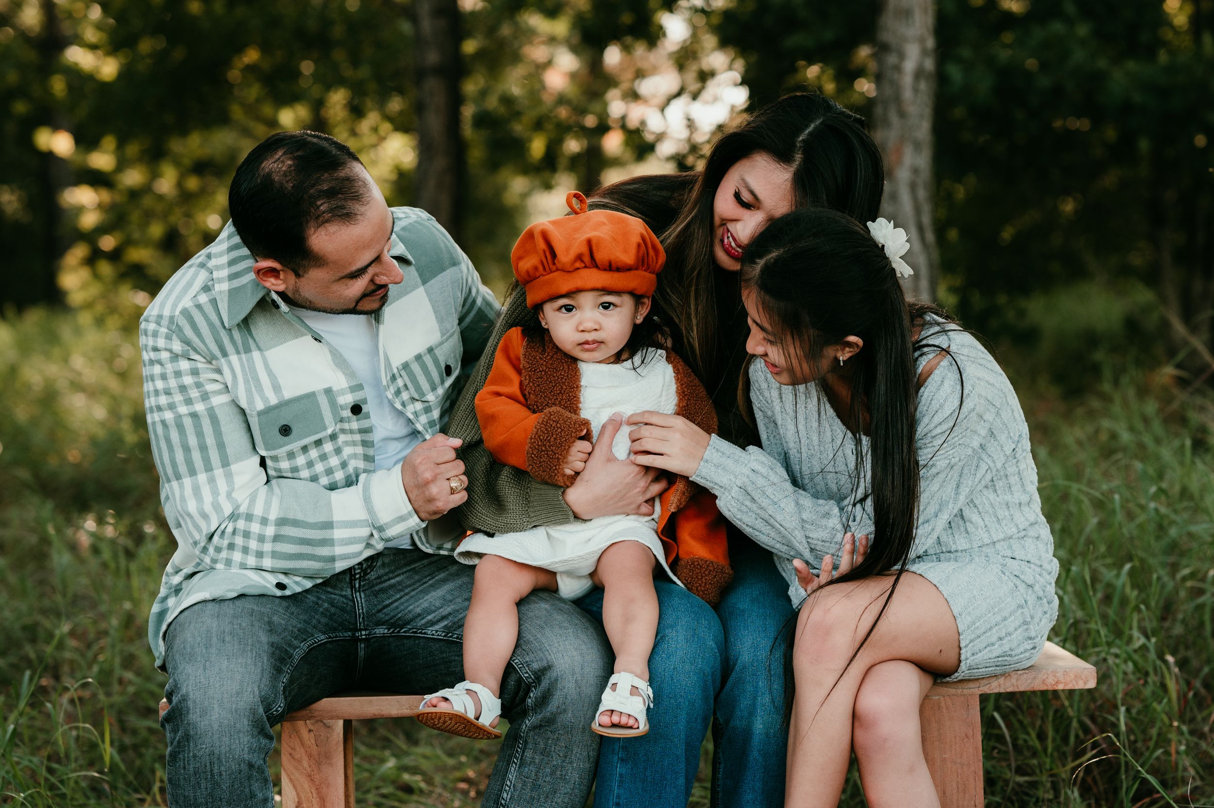 Family sitting together on a wooden bench during golden hour in a forest setting.