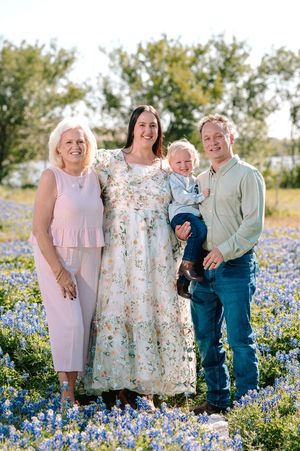 Family of four posing in a Texas bluebonnet field, featuring a grandmother, young couple, and baby boy.