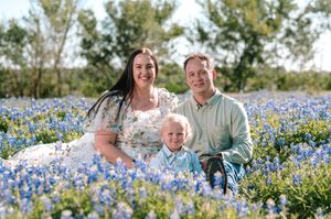 Family of three smiling in a Texas bluebonnet field on a sunny spring day.