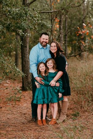 Family wearing coordinated green and black outfits poses in an autumn forest setting.