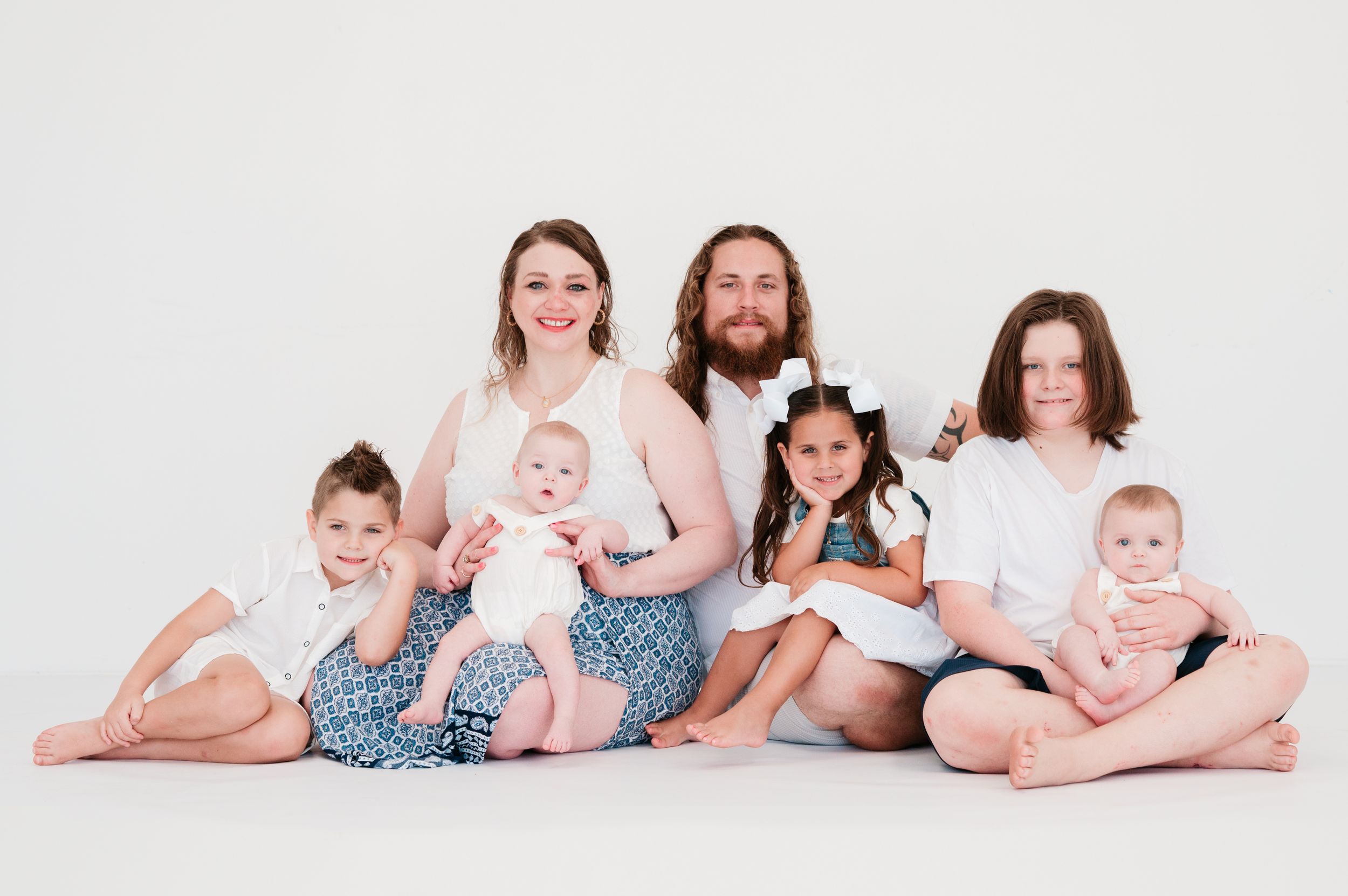 A family poses together in matching blue outfits against a white studio backdrop.