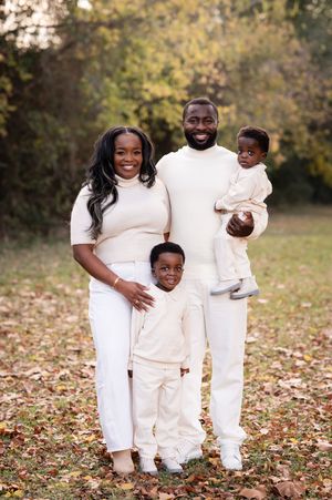 Happy Black family of four posing outdoors in matching cream outfits among autumn leaves in a park.