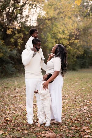A joyful Black family in matching white outfits poses outdoors among autumn leaves in a warm fall portrait.