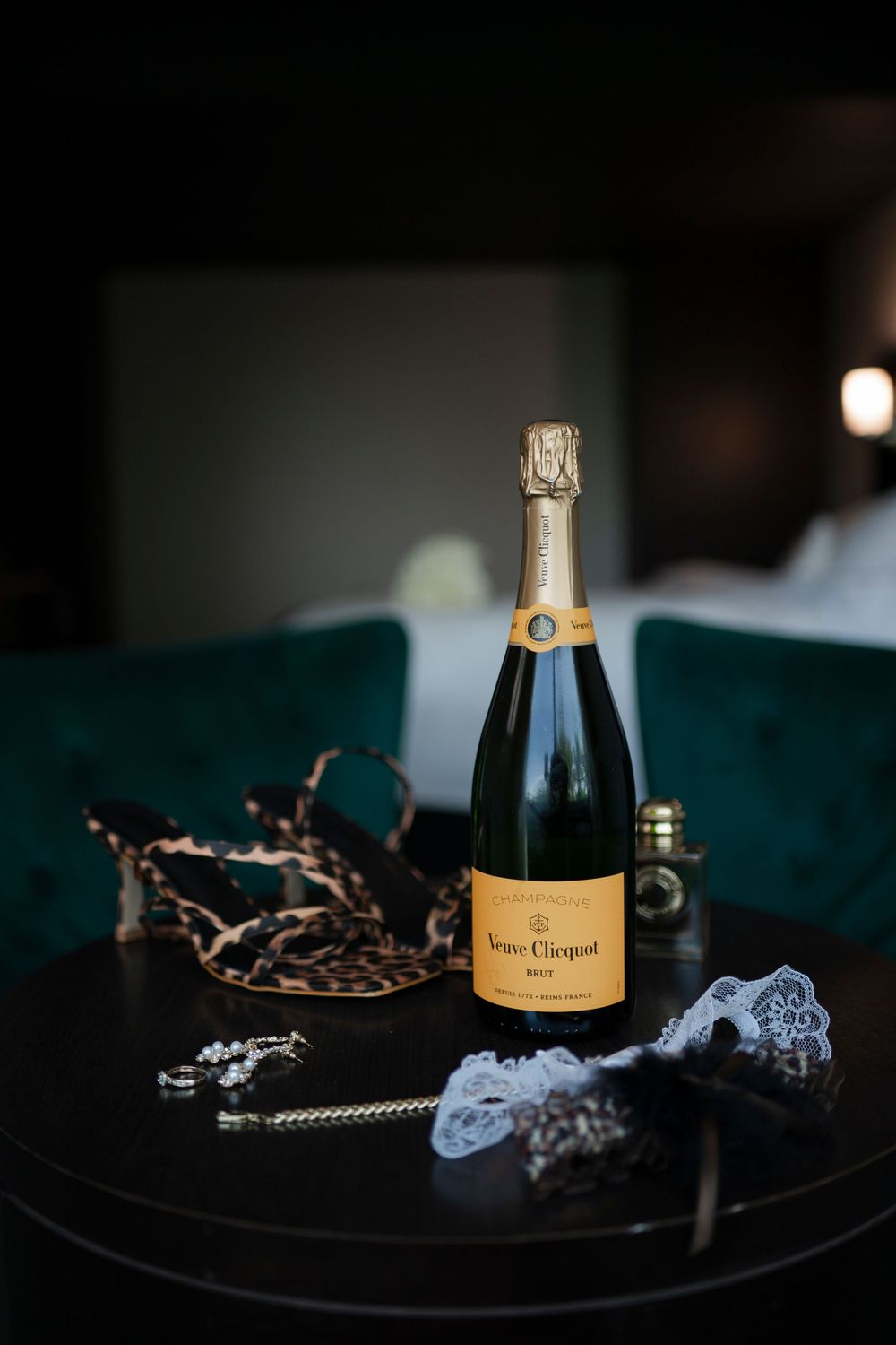 A bottle of Veuve Clicquot champagne sits elegantly on a dark surface with decorative lace and chain accessories.