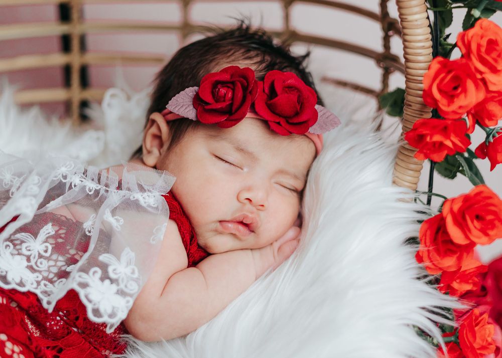 Sleeping newborn baby surrounded by vibrant red roses on white bedding.