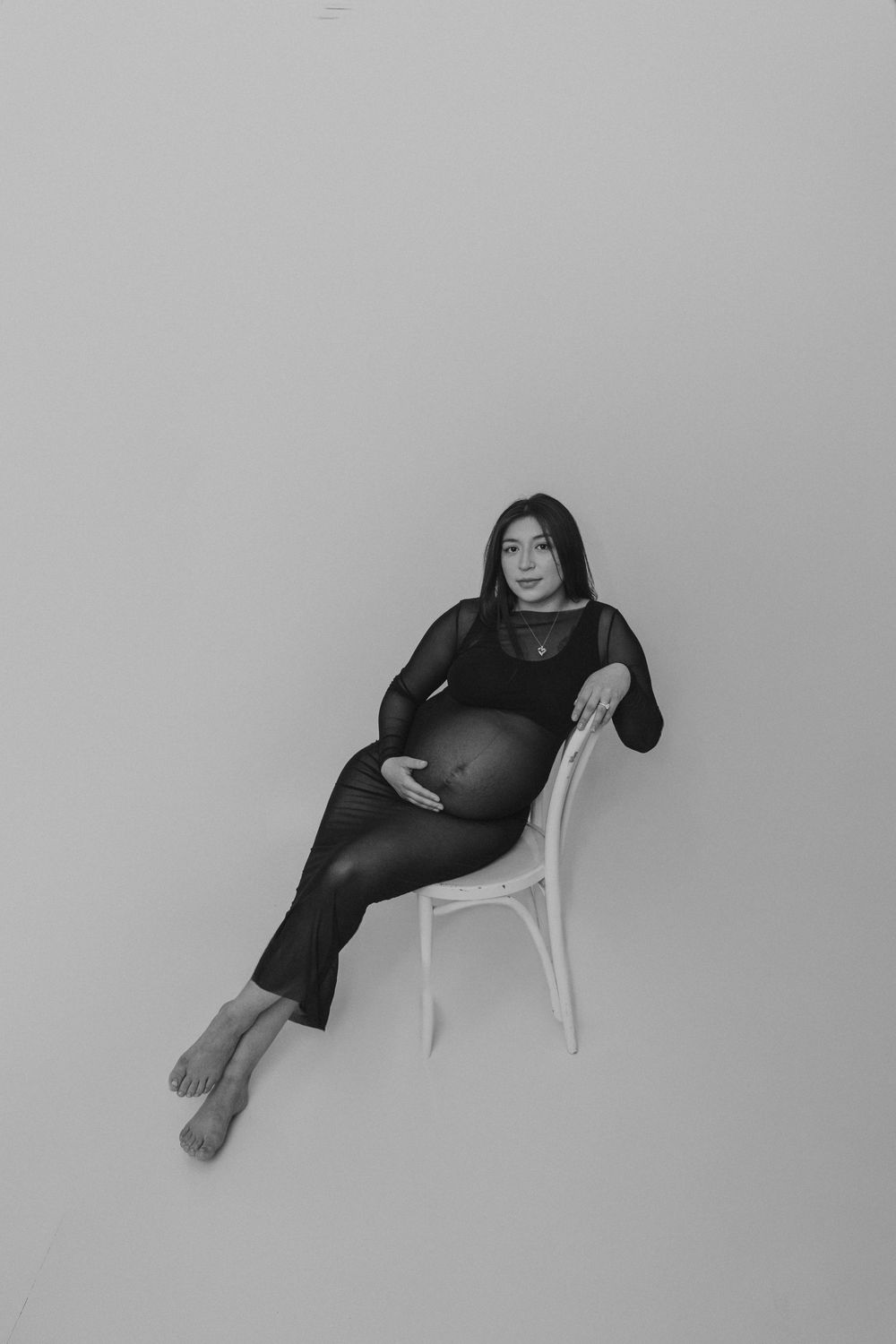 A minimalist maternity portrait in black and white showing a woman reclining on a chair.