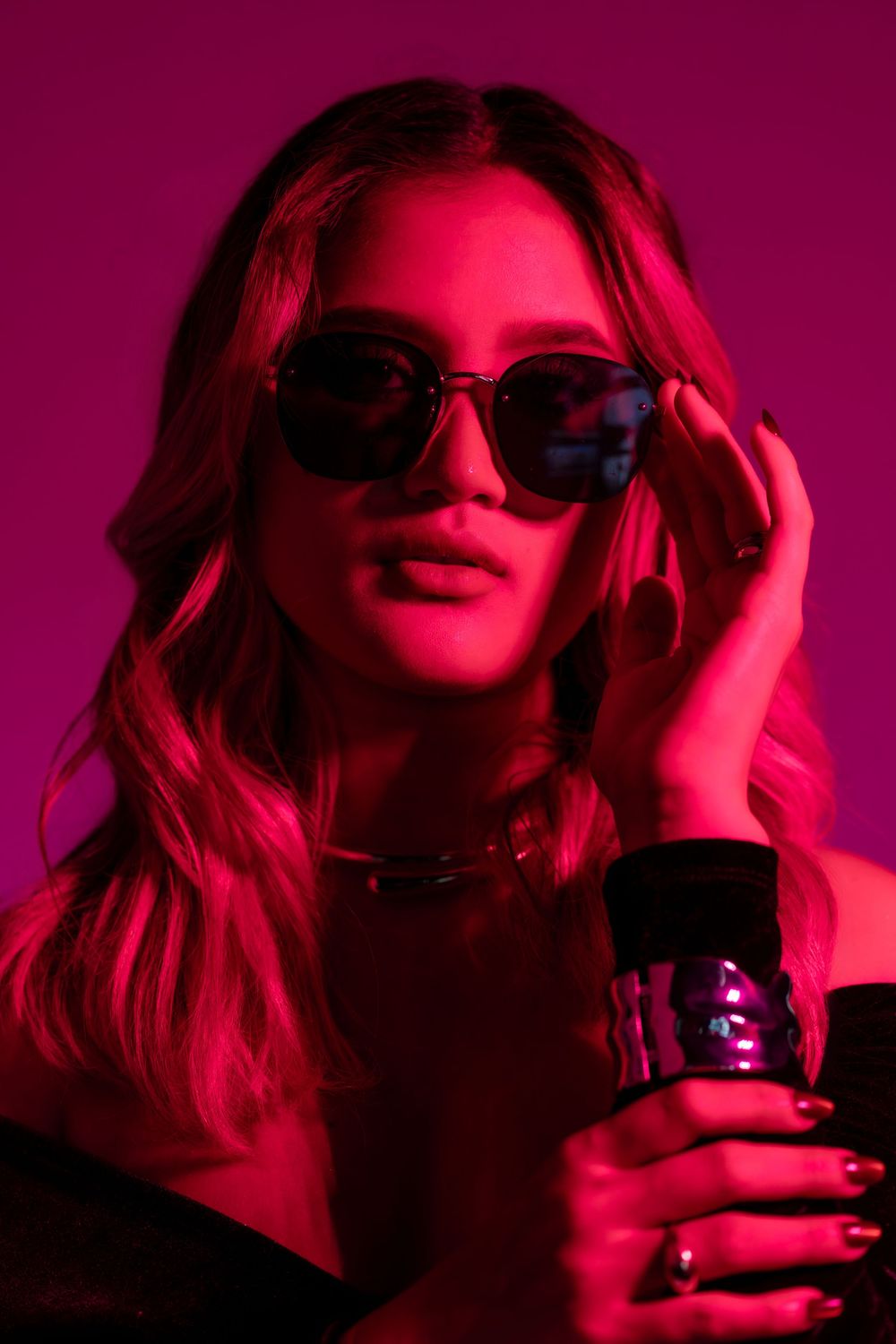 Person with blonde wavy hair wearing sunglasses in pink lighting holds a dark beverage glass in six sequential shots.