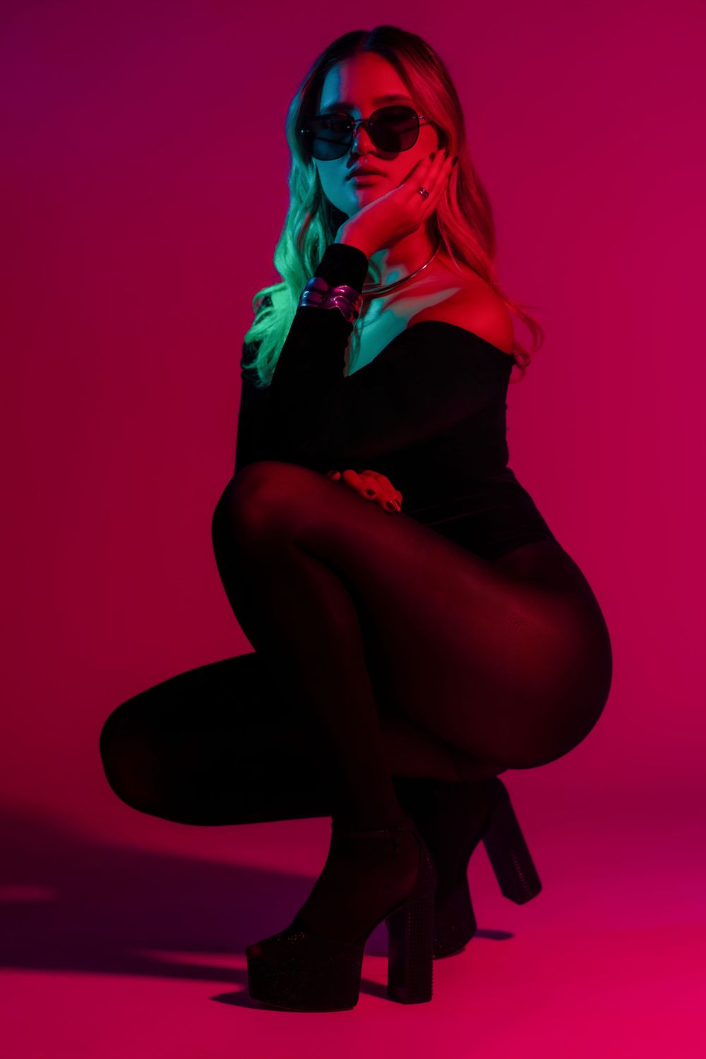 Silhouetted figure in black crouches against vibrant pink and turquoise gradient background with dramatic lighting effects.