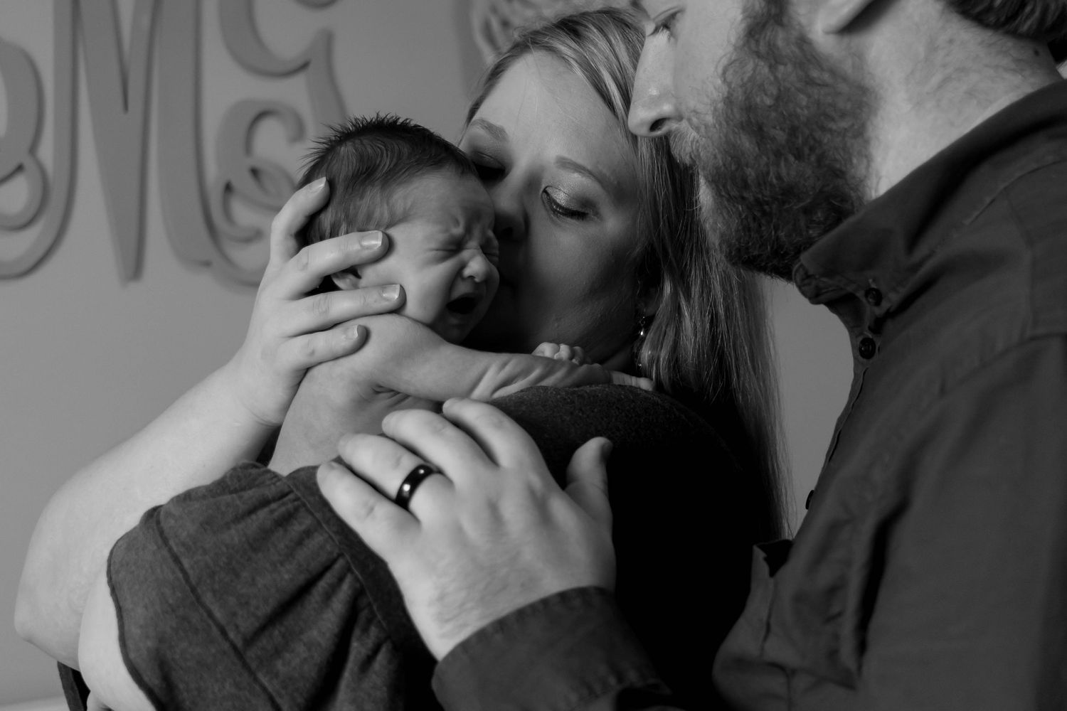 Intimate black and white portrait of parents kissing their newborn baby.