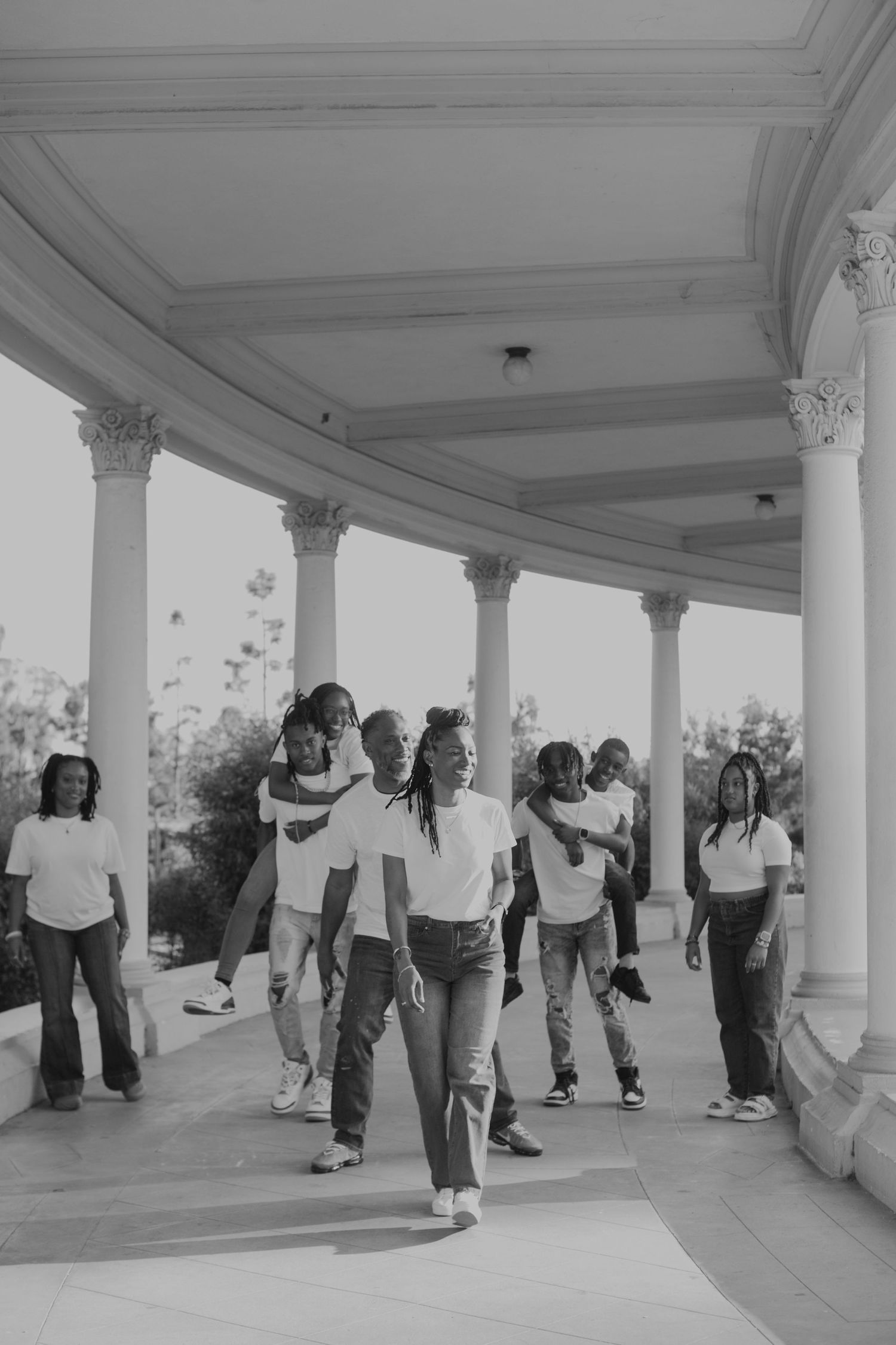 Group of people walking and interacting beneath a columned walkway in black and white.
