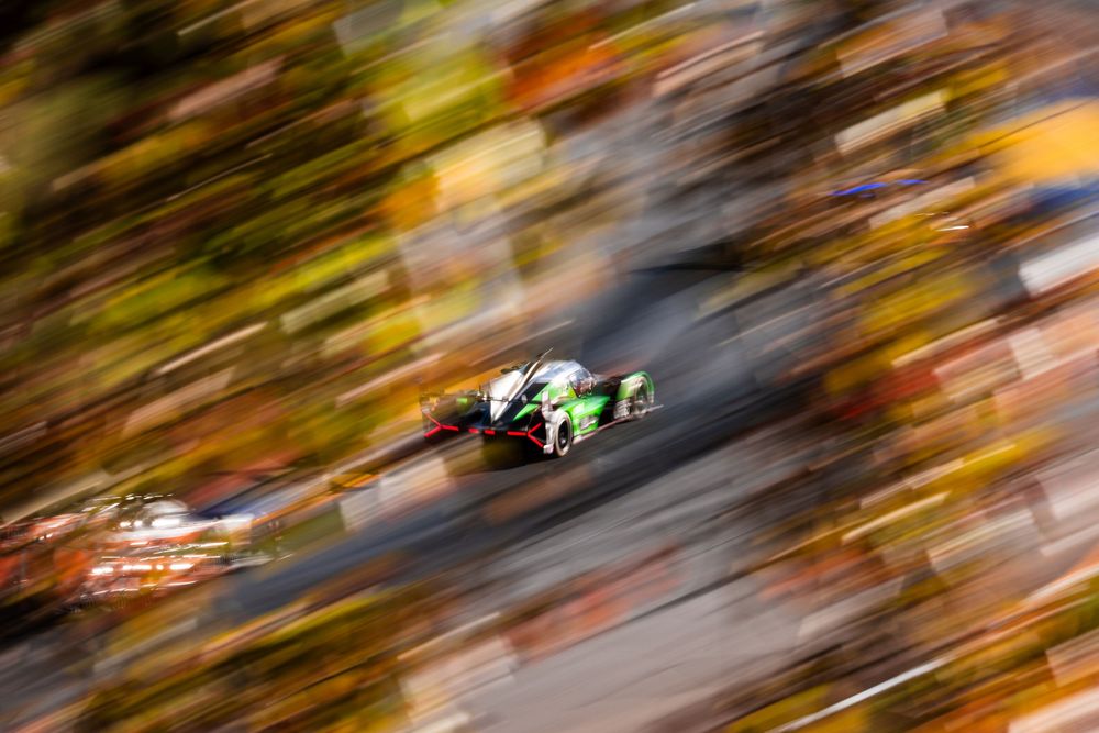 Race cars compete on a winding track with autumn foliage in the background.
