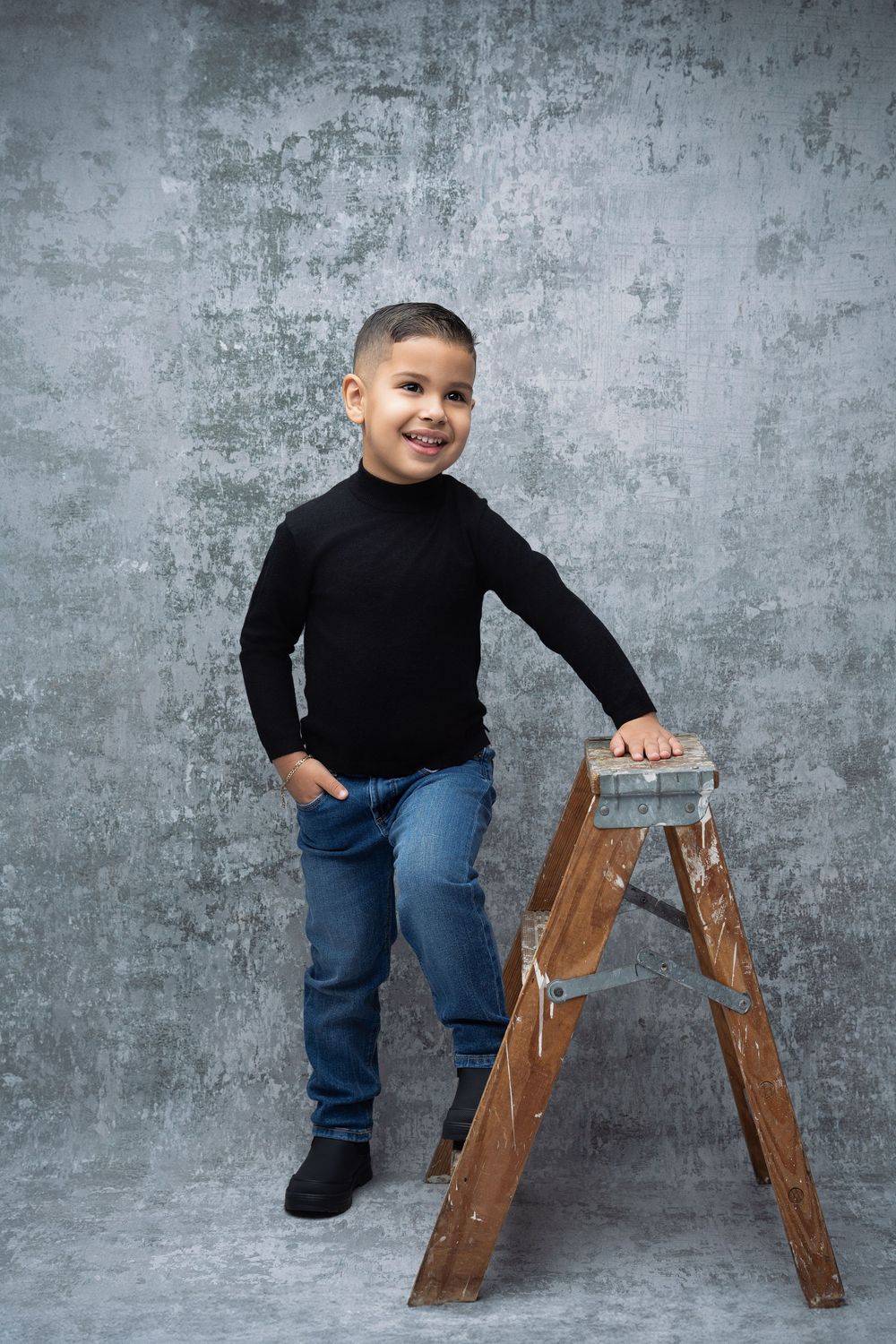 Miami Maternity photographer A child in a black sweater and jeans poses four different ways in front of a gray background