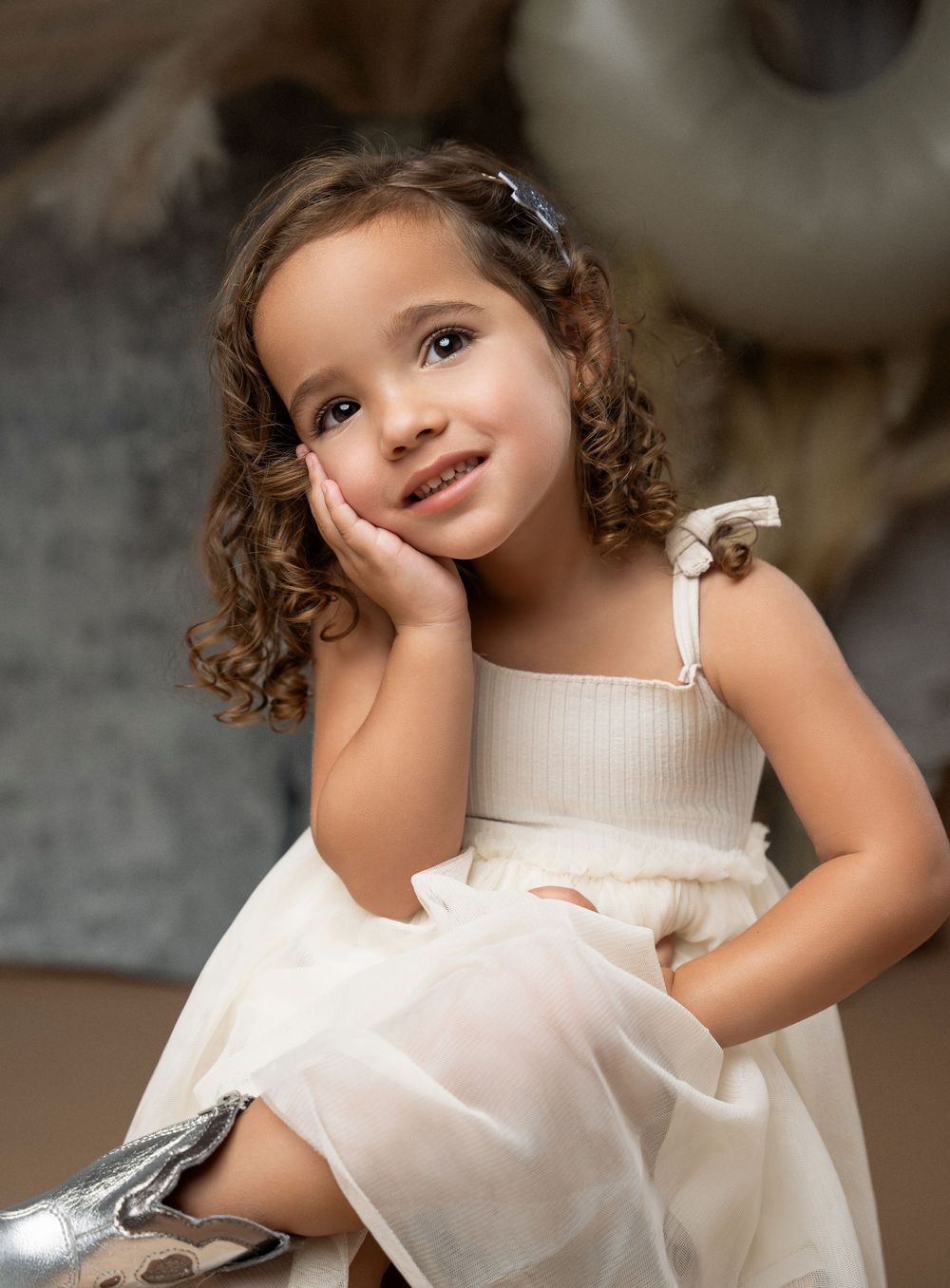 Miami Maternity photographer A child in a white dress twirls playfully while posing against a dark background in a classic portrait style.
