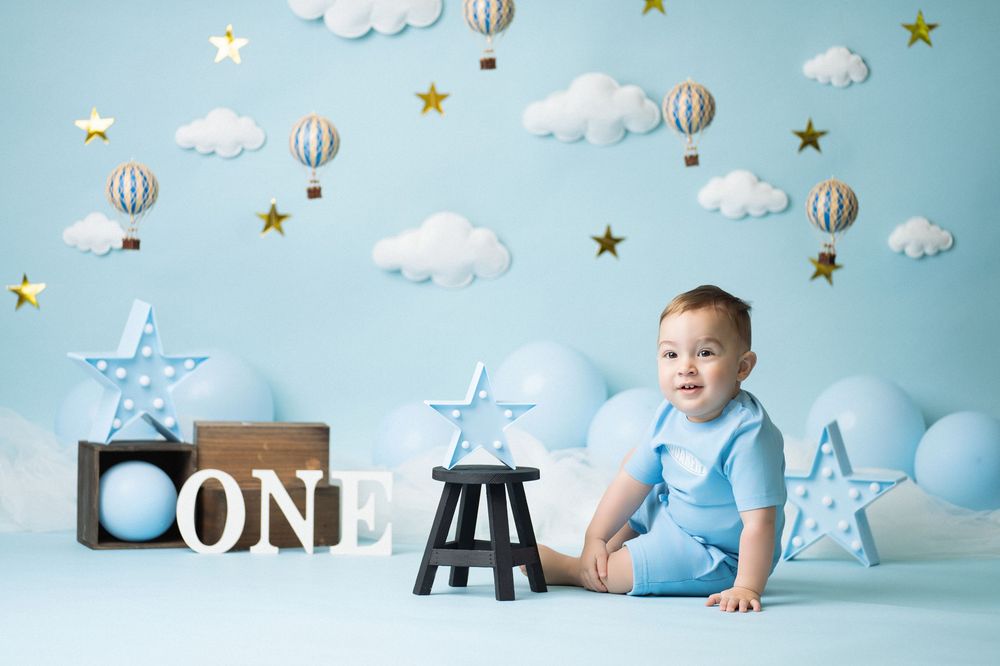 Miami Maternity photographer A baby in light blue clothing crawls on a decorated background with clouds, stars and hot air balloons.