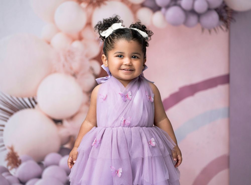 Miami Maternity photographer A little girl in a lavender tulle dress poses against a pink balloon backdrop for a birthday photoshoot.