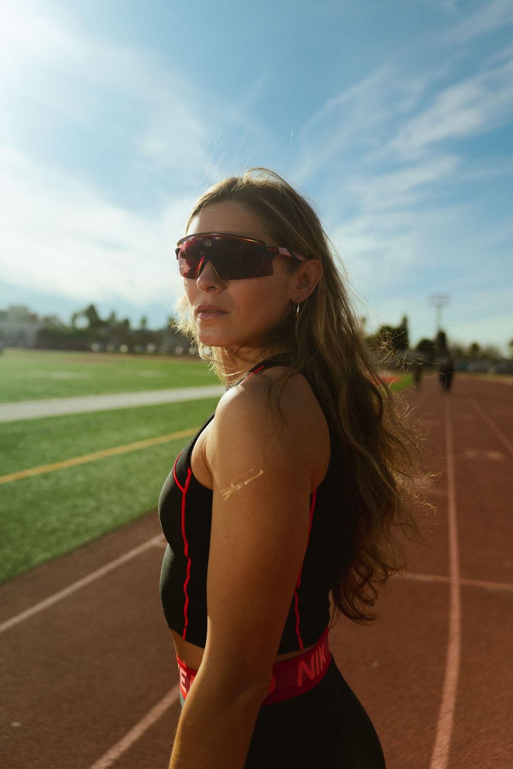 A female model poses in a track outfit with sunglasses on capturing a vibrant athletic track and field scene.