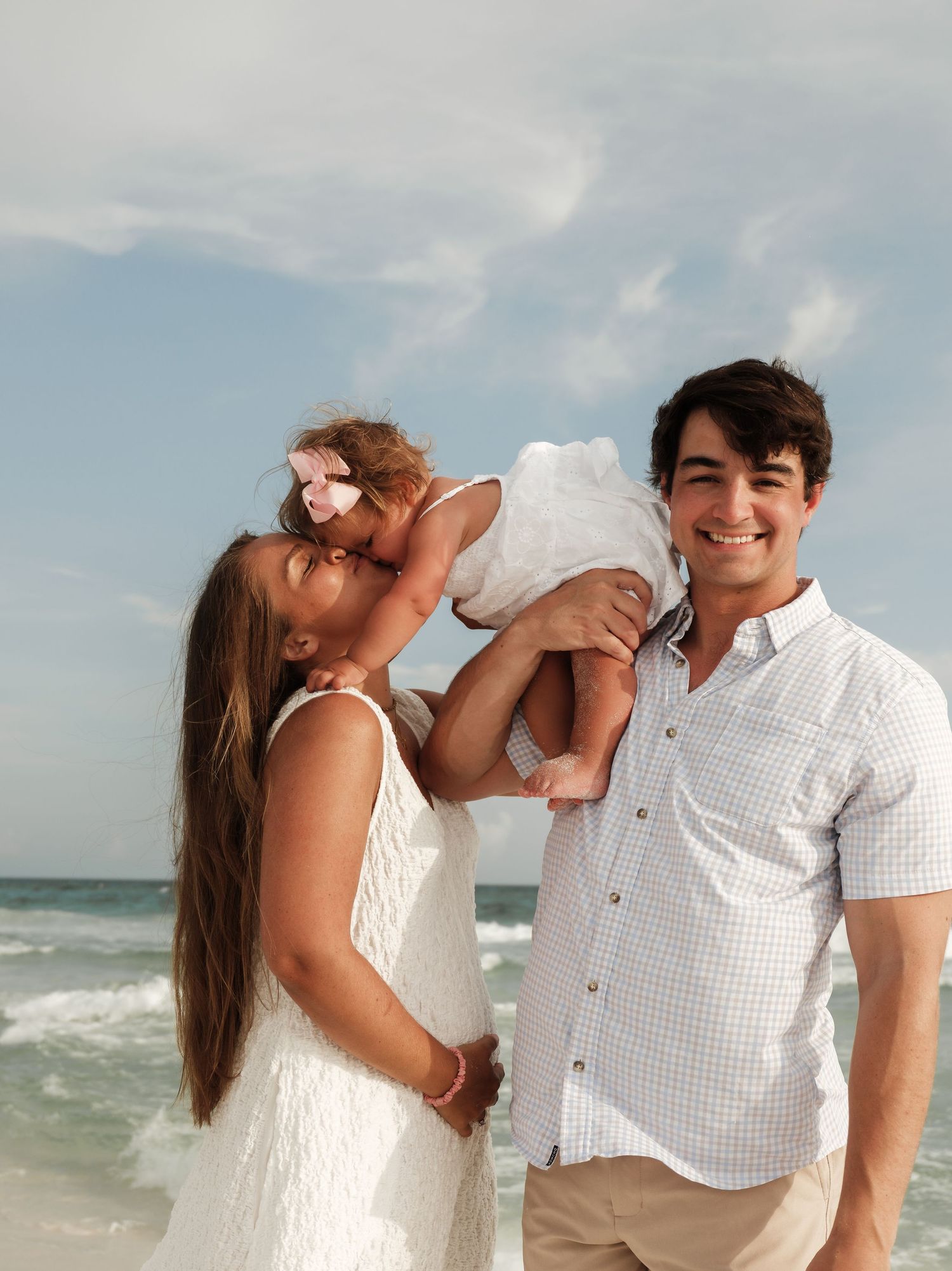 Family in white outfits sharing joyful moments on a breezy beach.