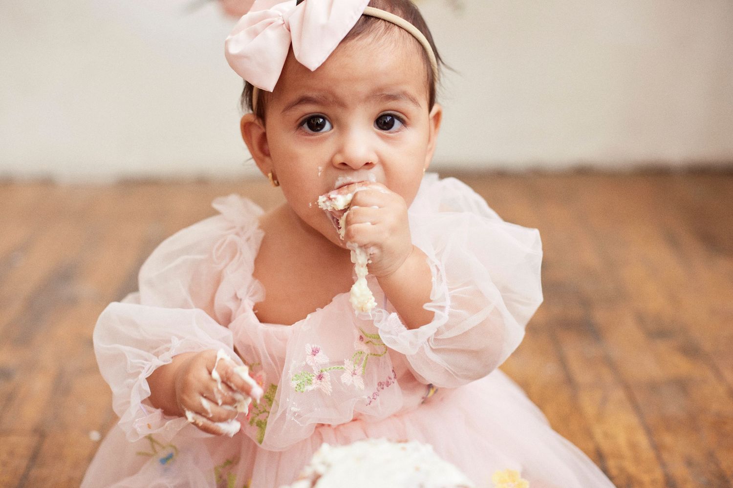 Baby in pink ruffled dress during first birthday cake smash photoshoot.