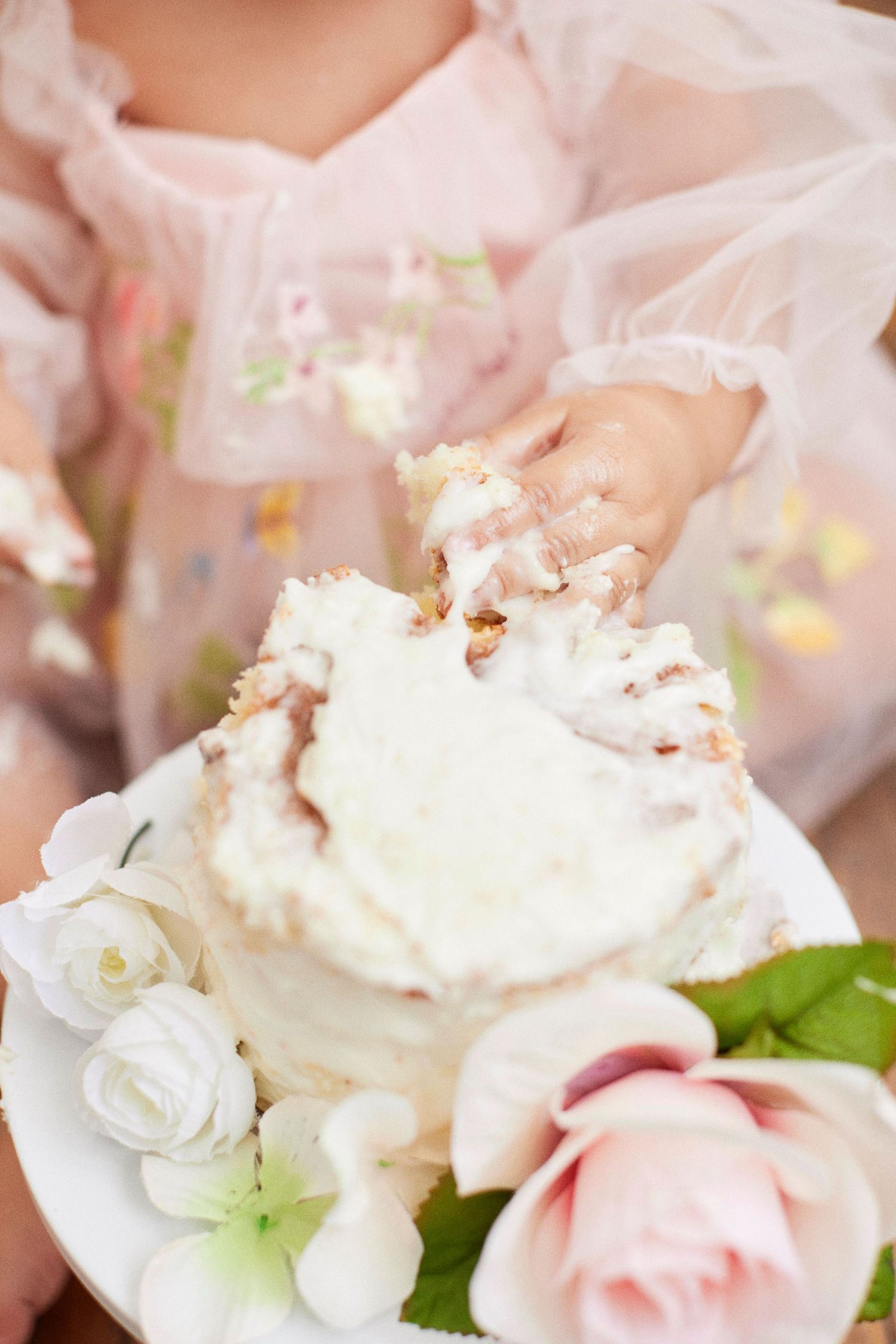 First birthday cake smash session with white frosting and pink floral decorations.