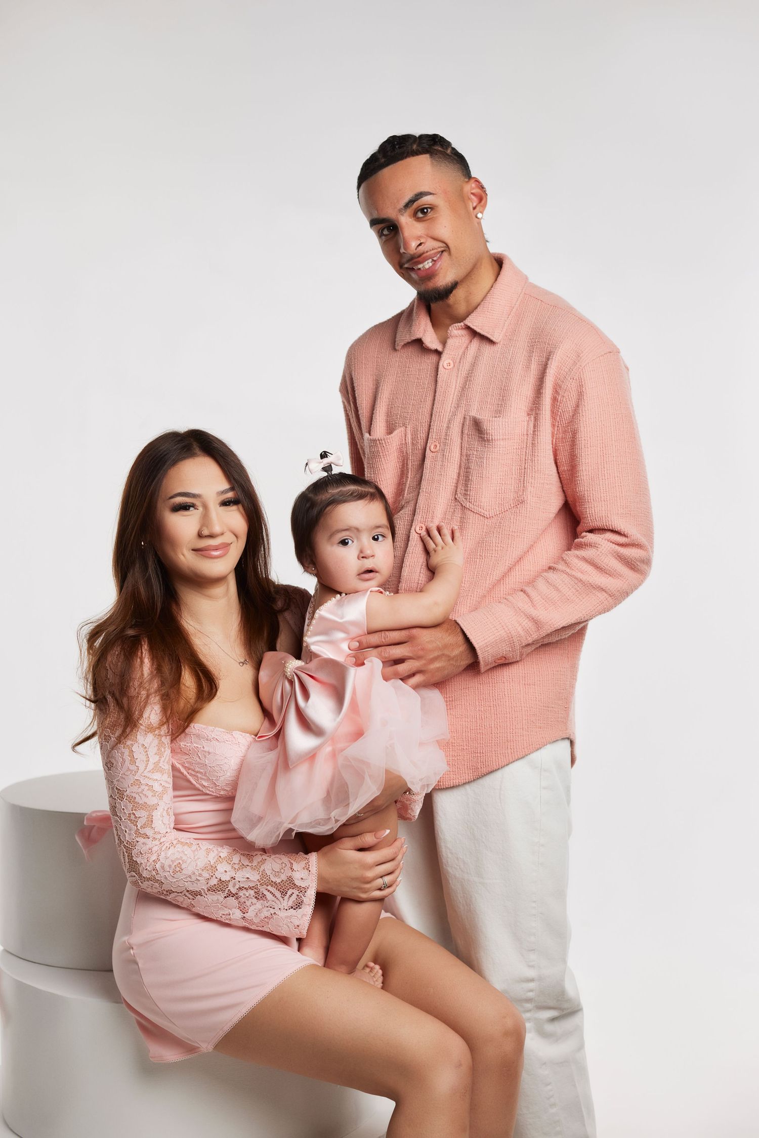 Family portrait session with coordinated pink and white outfits against light studio background.