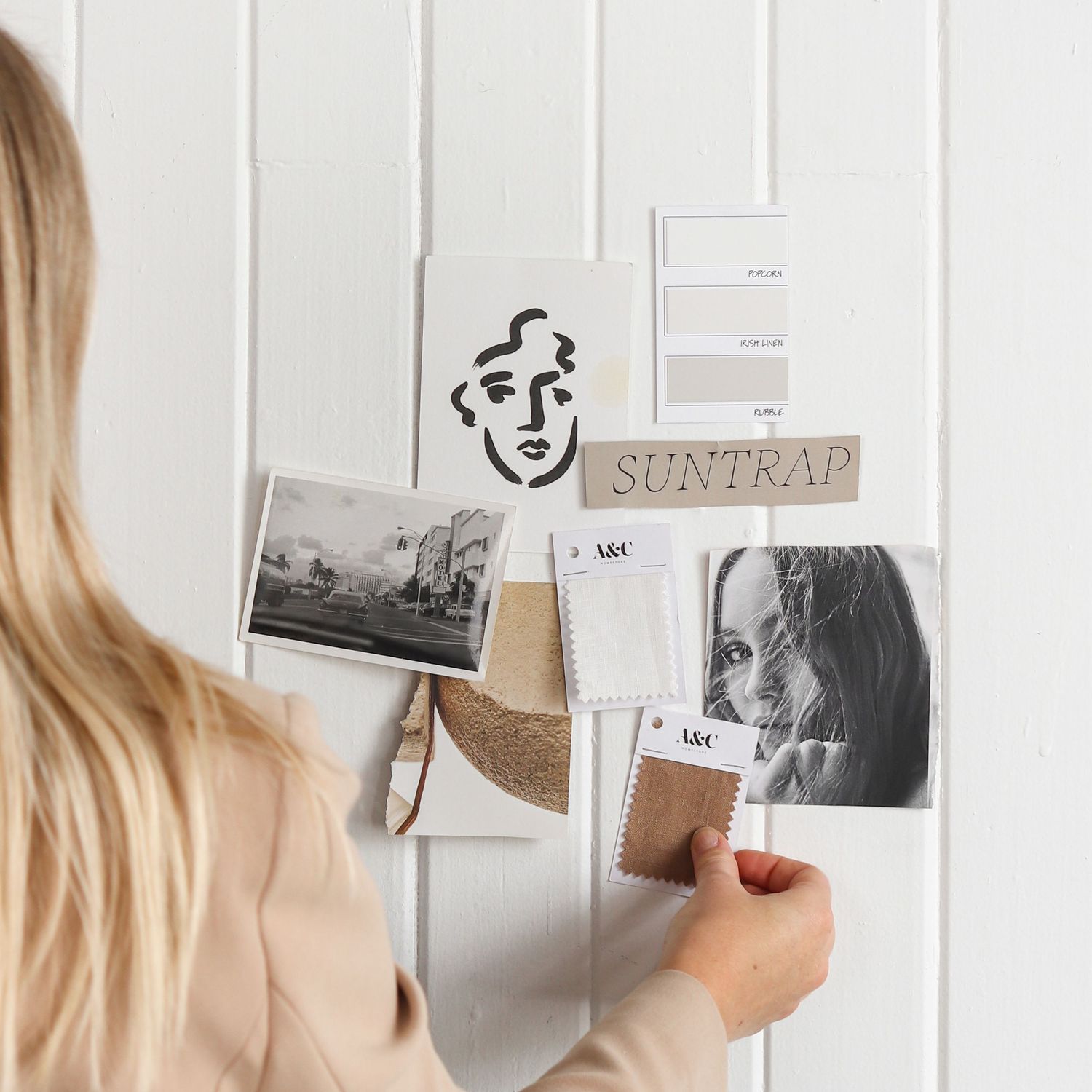Hand arranging black and white photographs on white wall display.