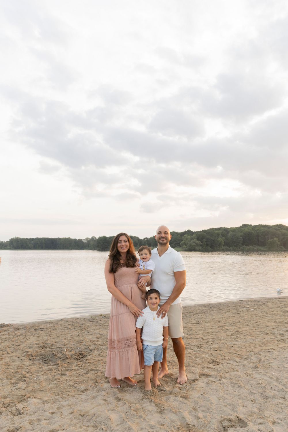 family of four smiling on the beach at stoney creek metropark wearing pinks, blues and whites