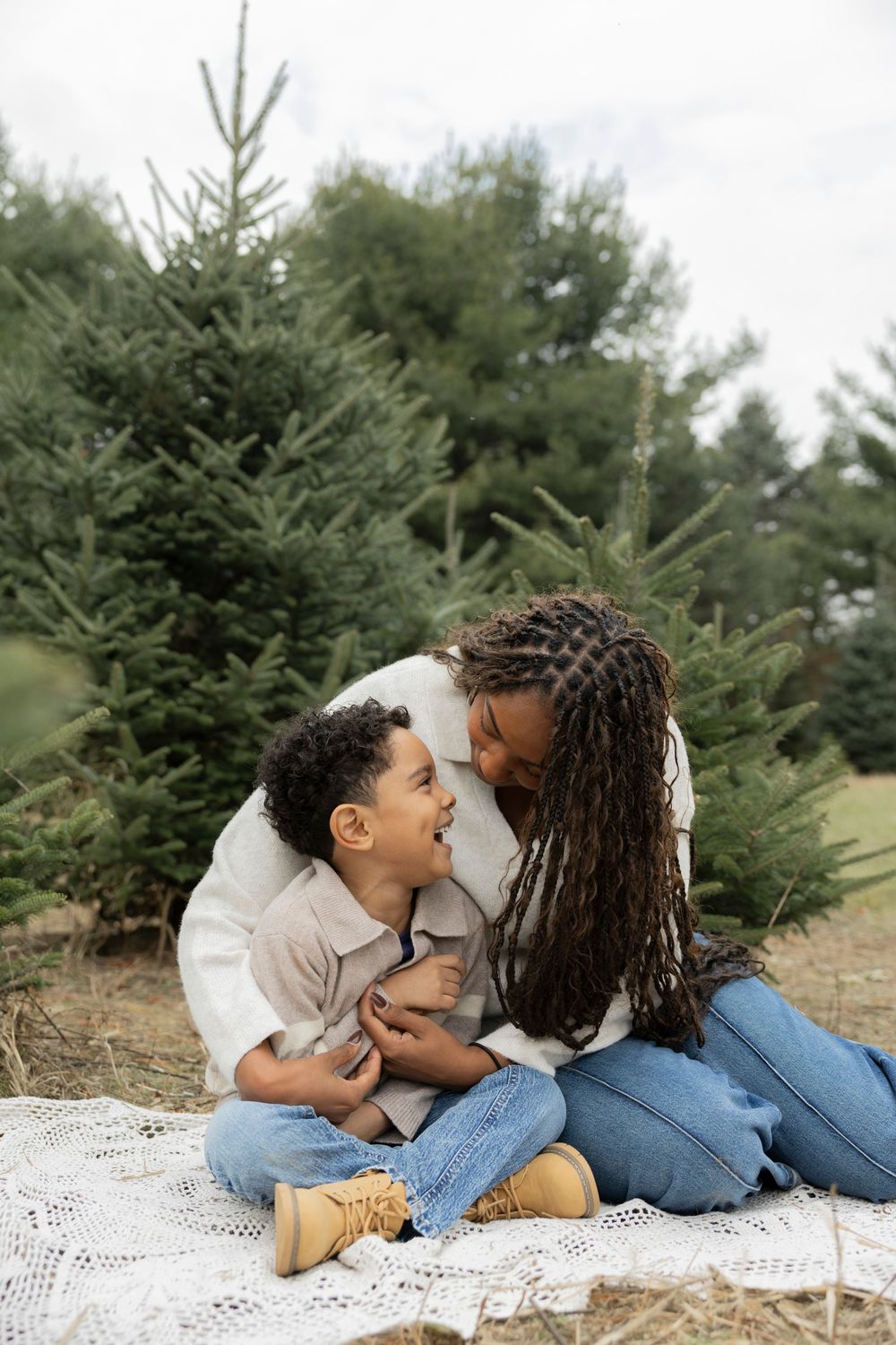 A loving family moment captured on a white blanket surrounded by evergreen trees in an outdoor setting.