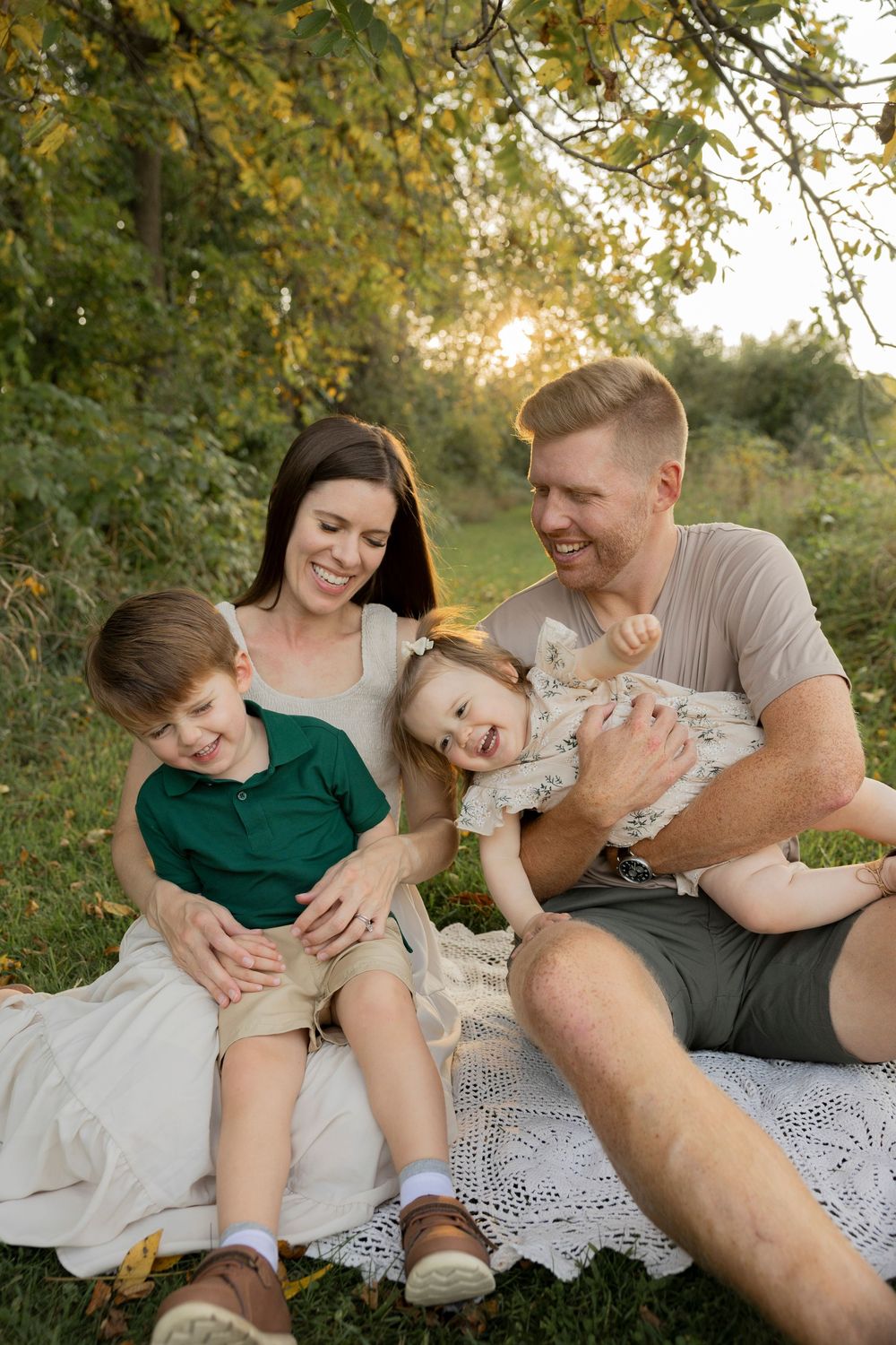 A playful family moment captured on a blanket outdoors during golden hour as a family laughs and cuddles together at troy farm park michigan