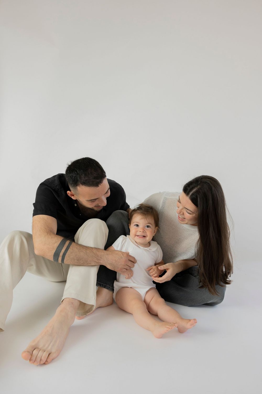 Family of three lying on white floor in casual clothing while playing and bonding together in studio setting in Oakland country Detroit