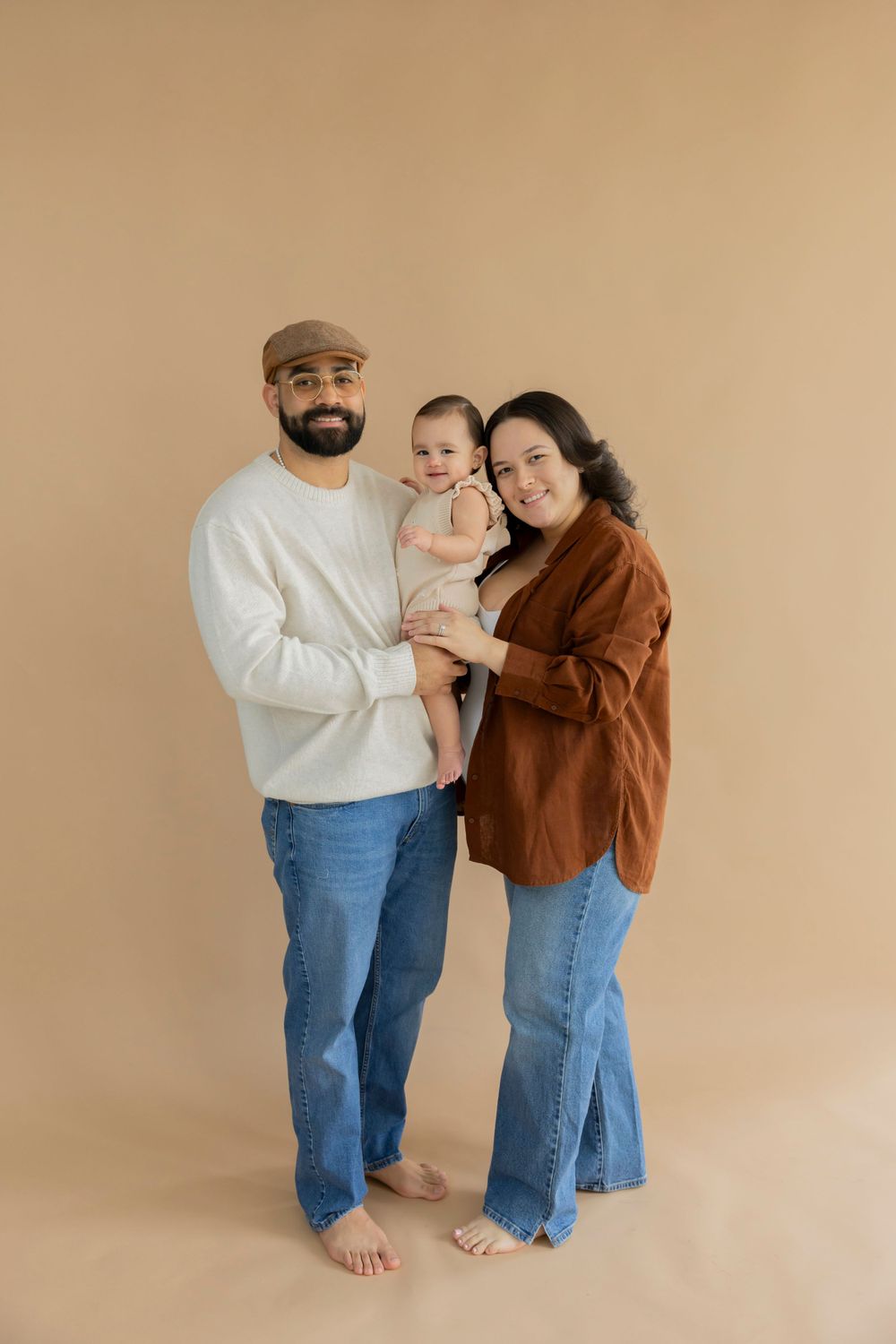 A family poses together barefoot against a beige background wearing casual denim and earth-toned clothing at LMP collective studio michigan