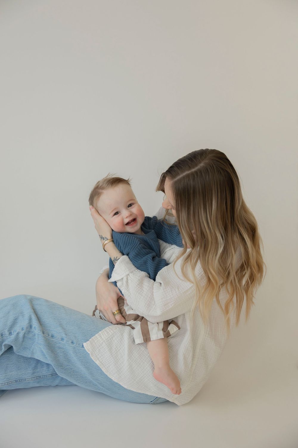 A tender moment between parent and baby wearing blue and white outfits against a white backdrop pin a studio in Metro Detroit Michigan