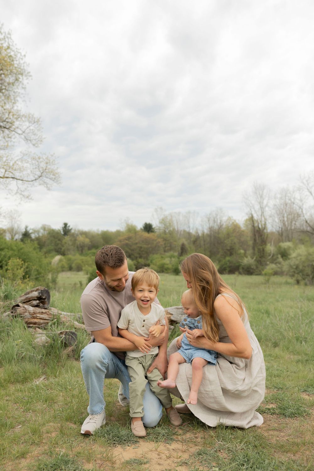 Happy family of four enjoying an outdoor photo session in a lush green meadow with trees in the background at troy farm park in michigan