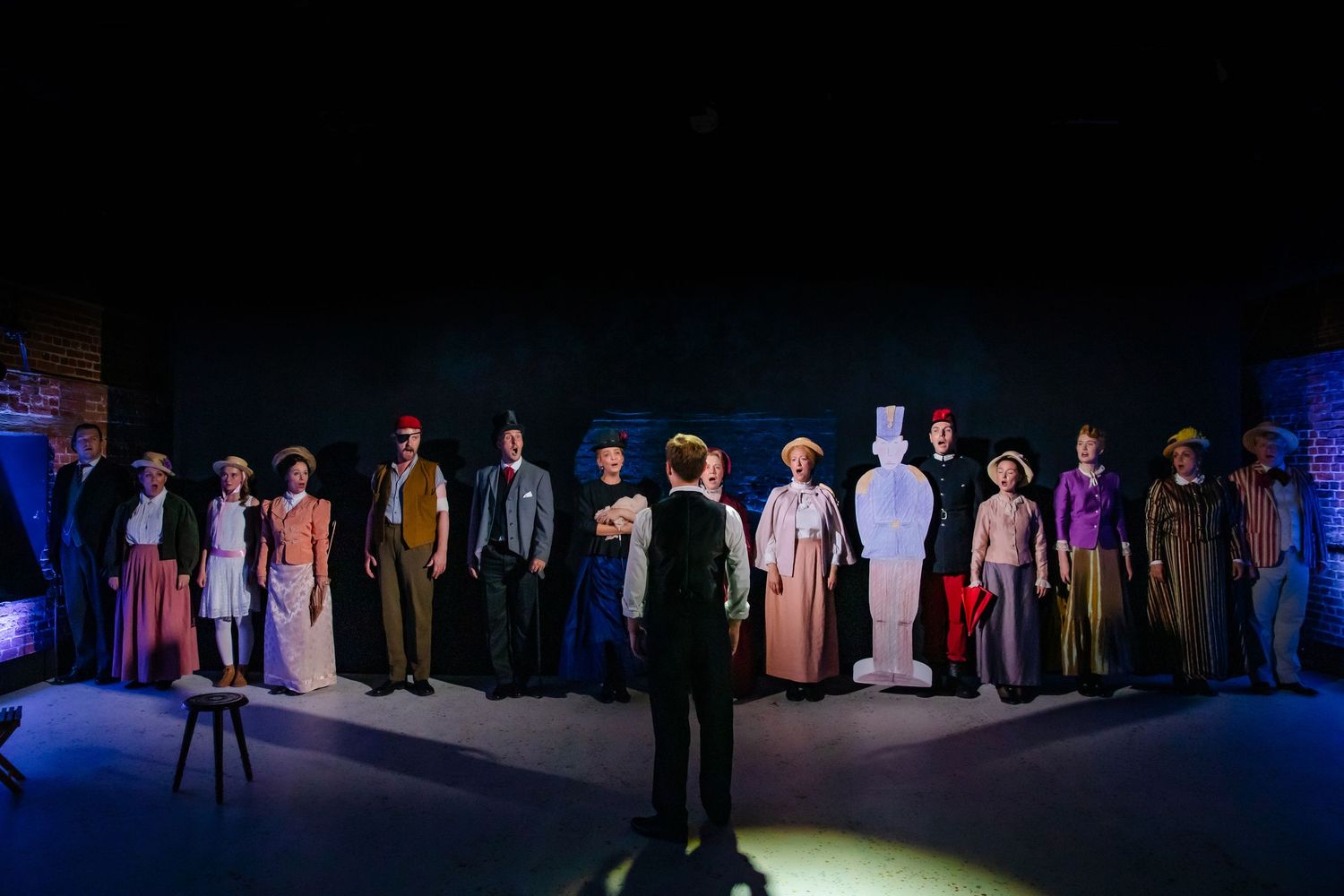 Theater ensemble stands in formation under dramatic lighting for group performance.