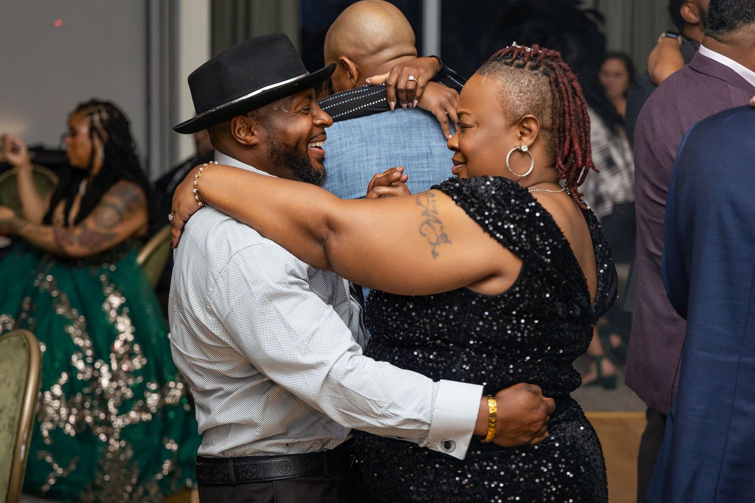 Couple sharing a joyful dance moment at an indoor event, with the dancer in white shirt and hat embracing their partner.