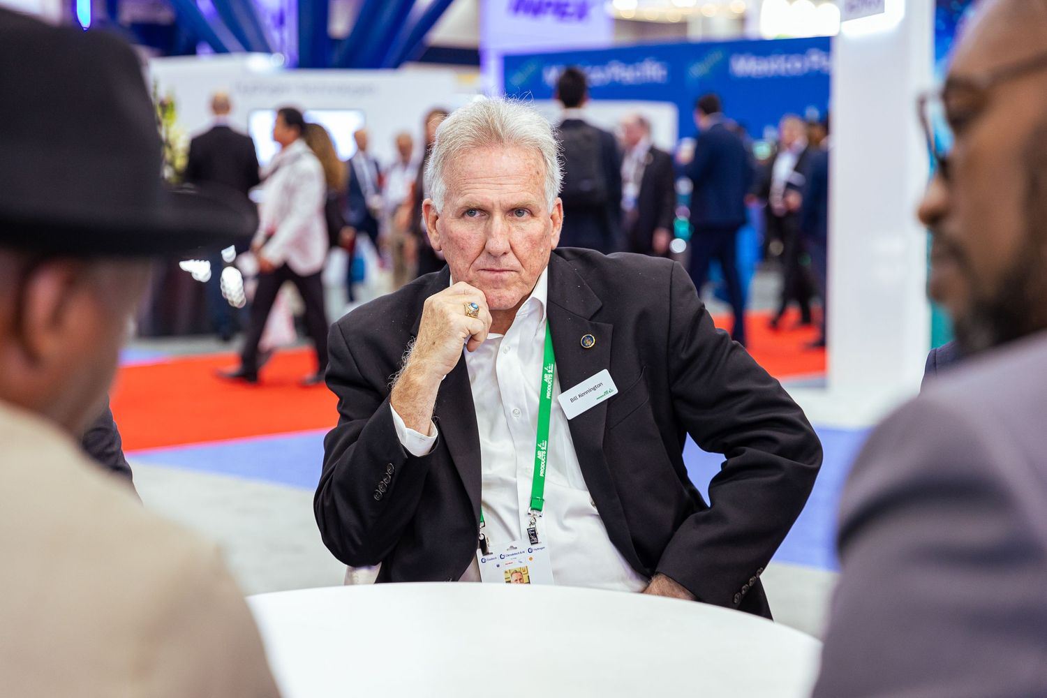 Man in suit gestures while talking to others at a business event.