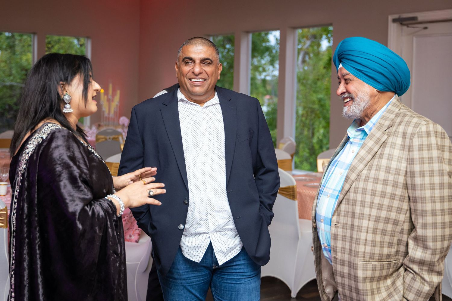Three people in formal attire engaged in conversation at an indoor event.