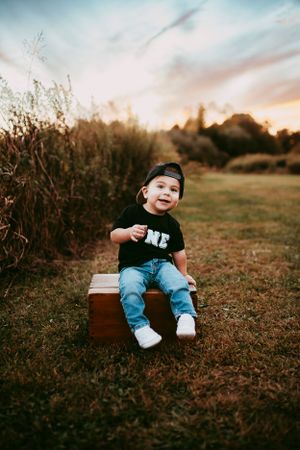 Toddler sitting on vintage suitcase in field during sunset photoshoot.