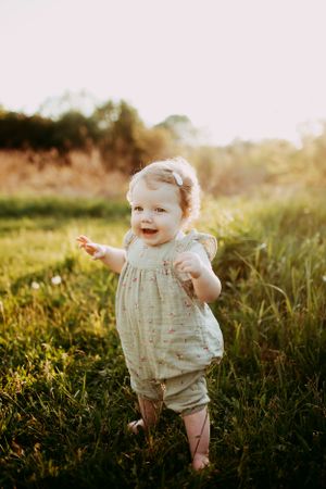 Baby in vintage romper laughing during golden hour outdoor photoshoot.