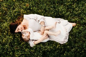 Child in white dress lying in green grass during outdoor portrait session.