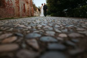 Low angle view of a cobblestone path leading to a couple standing by an old brick wall on their wedding day.