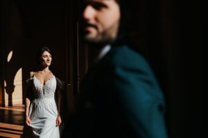 Artistic wedding photo with bride in white dress in background and silhouette of groom in blue suit in foreground.