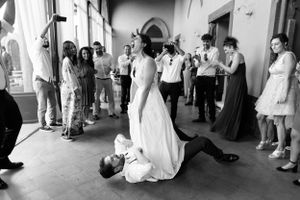 Black and white photo showing a playful group dancing at a wedding reception in an indoor venue with guests watching.