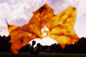 Silhouettes against a sunset sky viewed through a glowing autumn maple leaf with sun peeking through.