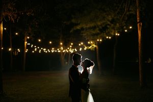 String lights illuminate a romantic outdoor wedding ceremony path through trees at night.