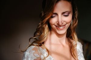 A smiling bride wearing a lace wedding dress looks down with natural light illuminating her glowing expression.