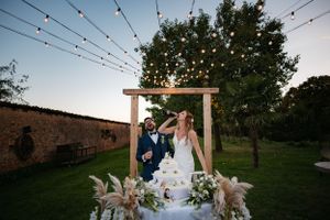Outdoor wedding reception setup with wooden arch, string lights and floral arrangements in a garden setting at dusk.