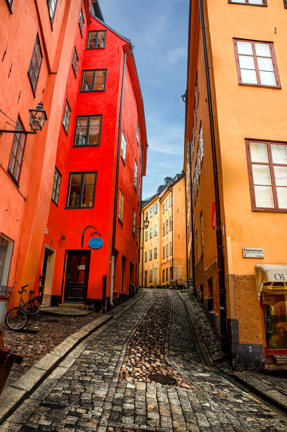 Narrow cobblestone alley between colorful red and orange historic buildings in Stockholm's old town district.