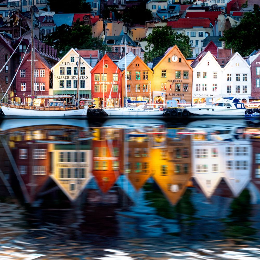Colorful historic buildings reflecting in calm harbor waters at twilight in Bergen, Norway.